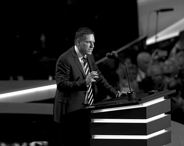 Peter Thiel in a dark suit while giving a speech at a podium.